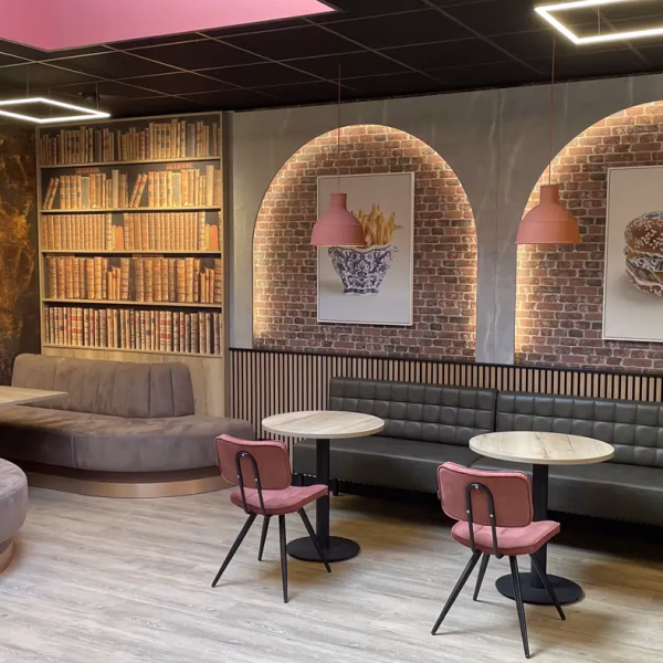 Interieurontwerp en styling van het loungecafé in het Damstede Lyceum, met maatwerk zitbanken, ronde tafels en warme materialen.